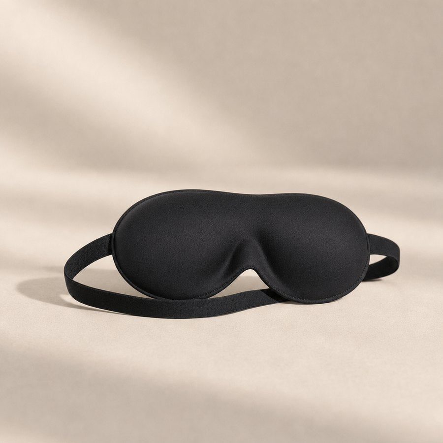 A soft black contoured sleep mask with a flat elastic strap